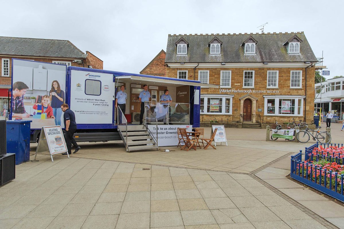 Lewington Heating staff engaging with visitors at a Worcester Bosch exhibition trailer event in a town square, promoting heating services.