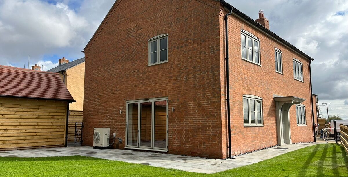 Exterior view of a newly built red brick house with a neat garden and an air source heat pump discreetly installed at the side.