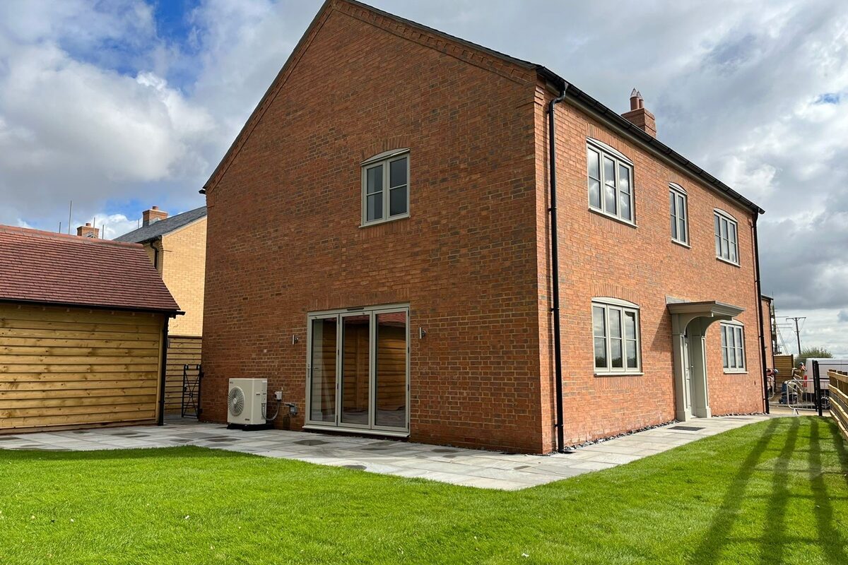 Exterior view of a newly built red brick house with a neat garden and an air source heat pump discreetly installed at the side.